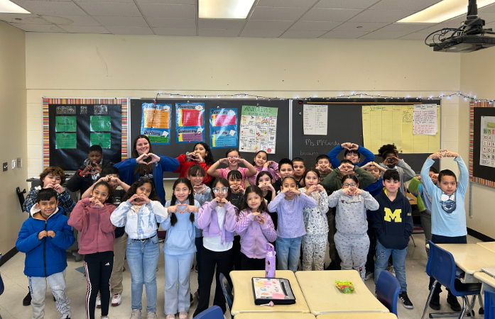  Ms. Y holding and a 3rd grade class smiling and holding up heart hands